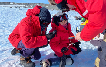 A group of researchers in red parkas collecting a meteorite.